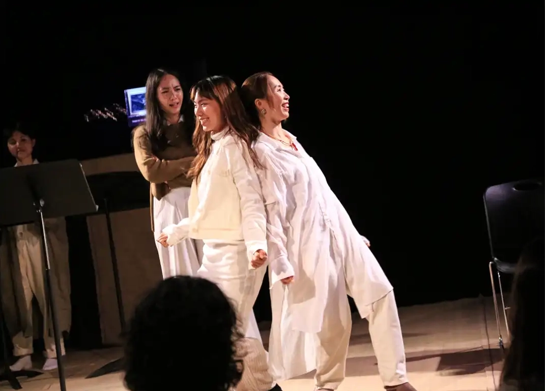 Two characters smile and lean on each other's backs while observed by third character in the background